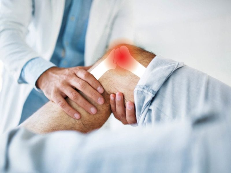 A doctor examining a patient's knee with a highlighted red area indicating joint pain or arthritis.
